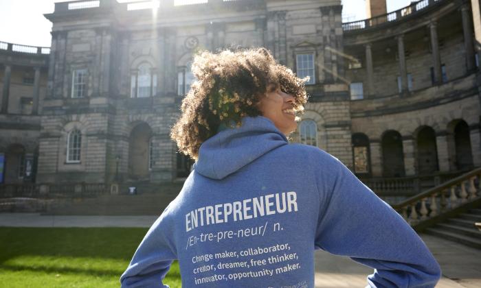 A young woman stands in front of Edinburgh's university building with her back to the camera, wearing a hoodie emblazoned with the word 'Entrepreneur'